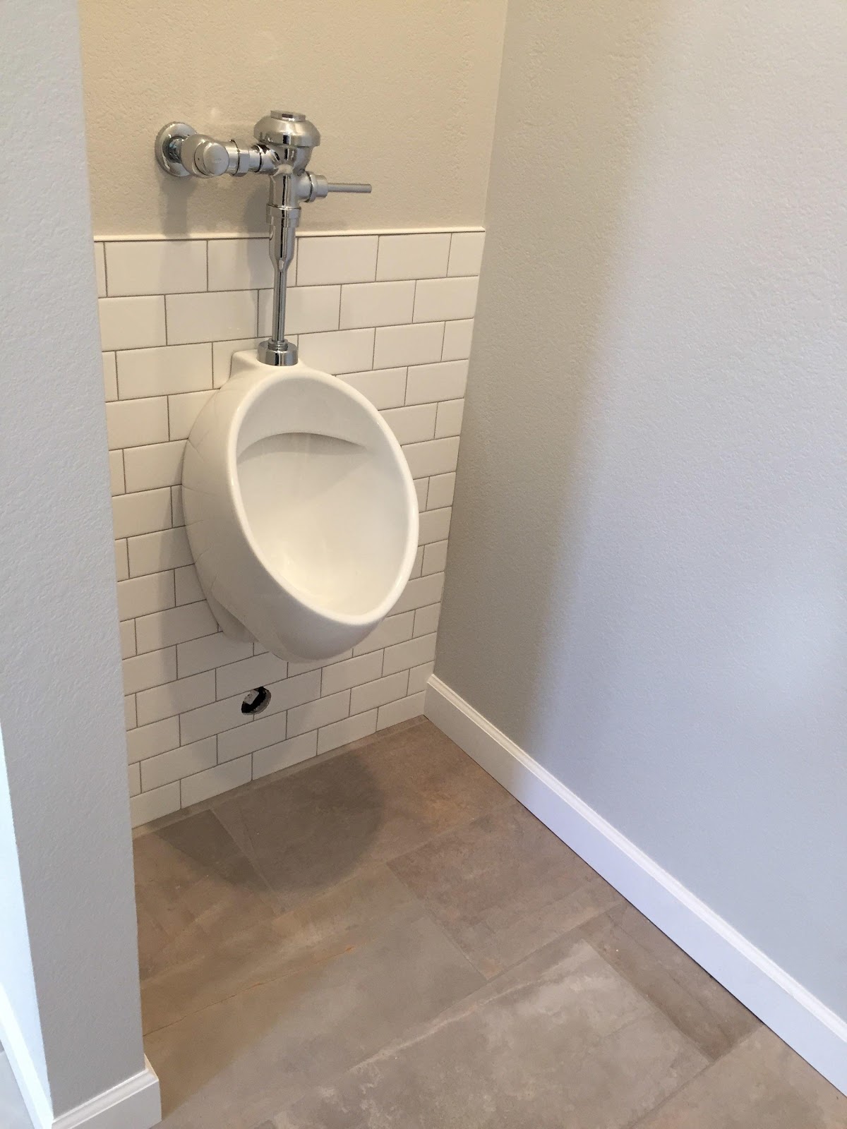 Wall-hung urinal with a chrome flush valve on white subway tile